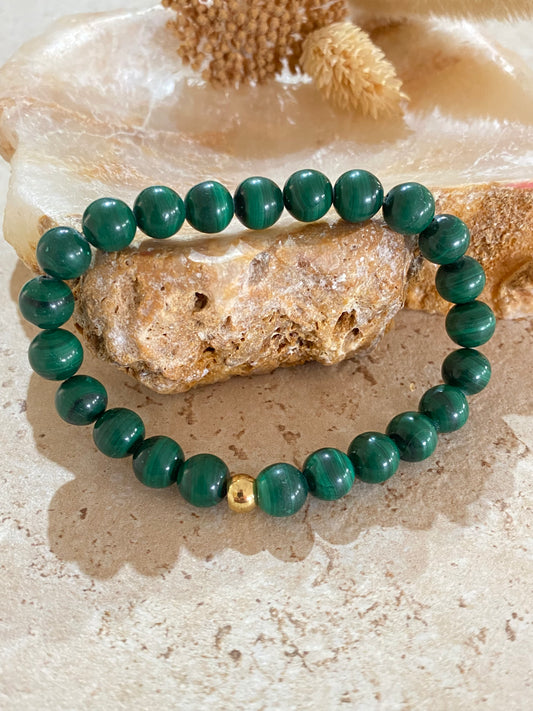 Bracelet en perles de malachite verte naturelle avec perle dorée, posé sur pierre minérale