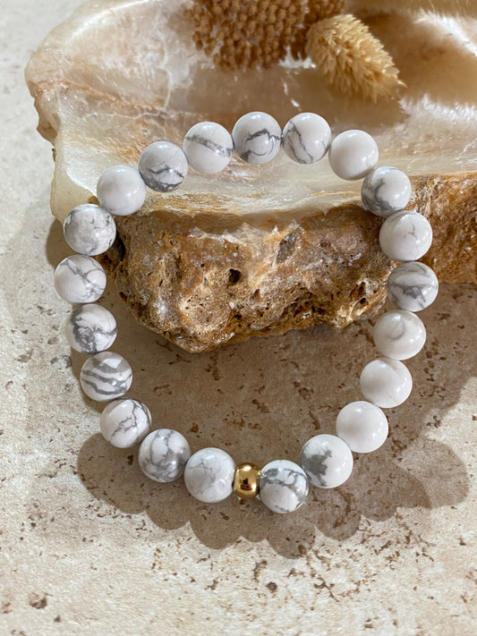 Bracelet perles rondes howlite blanche et perle dorée, posé sur pierre minérale décorative